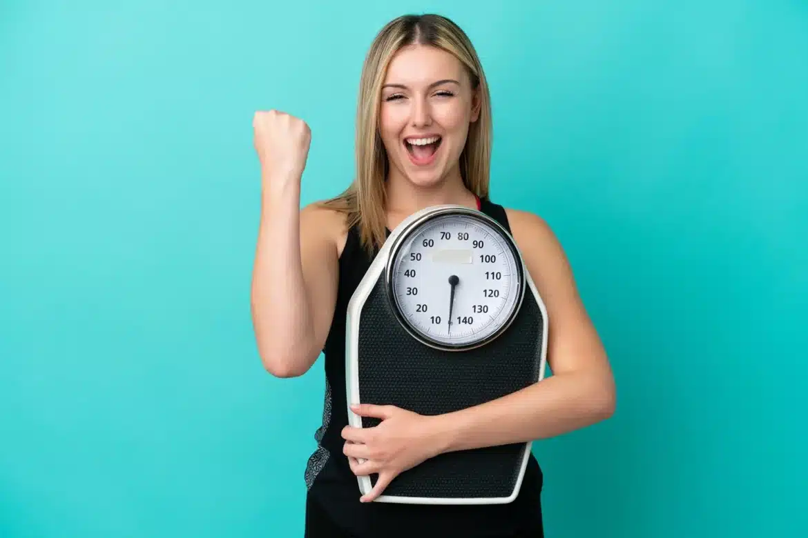 Femeie fericită ținând un cântar, simbolizând succesul în scăderea în greutate după gastric sleeve