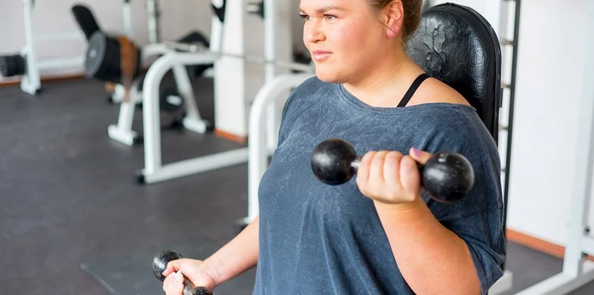 Femeie supraponderală efectuând exerciții cu gantere într-o sală de fitness, ca parte a procesului de schimbare a stilului de viață după chirurgia bariatrică